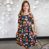 Young girl wearing a dress with cat pattern against a white wall.
